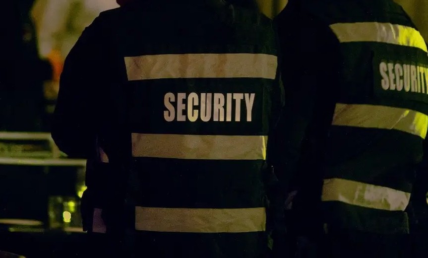 Security personnel, embarking on promising security careers, are standing in a dimly lit area, their jackets boldly emblazoned with "SECURITY" on the back.